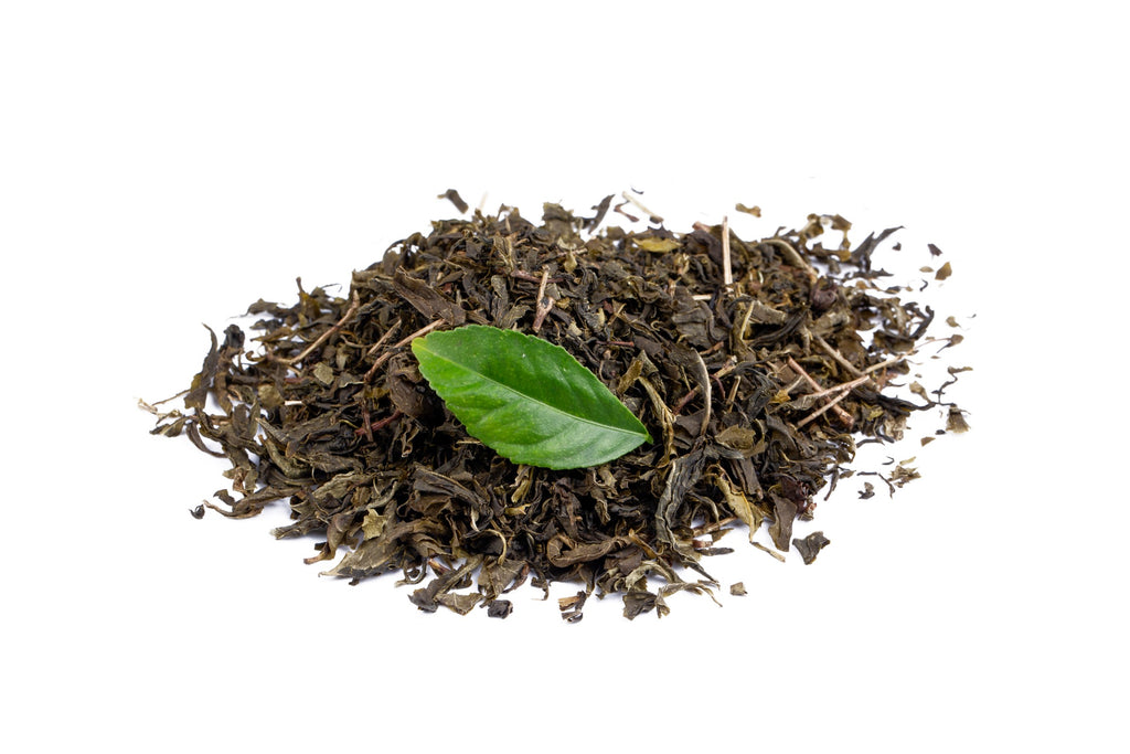 A live green tea leaf resting on a small pile of dried black tea leaves