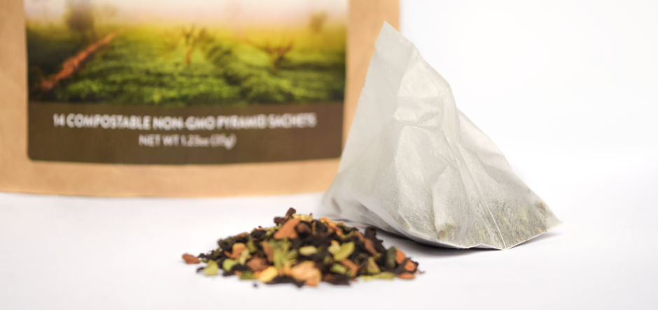 Closeup image of a loose leaf tea blend next to a tea sachet.  In the background is the blurred bottom section of the outer packaging of one of Aretea's products.